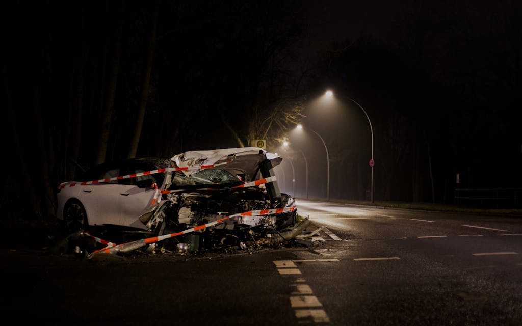 A wrecked car after a 18-wheeler accident crash on a dimly lit highway in Texas at night. Reviewed by and 18-wheeler accident lawyer.